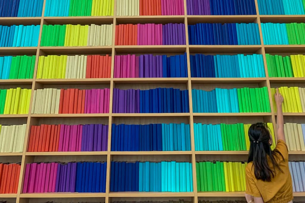 a photo of a woman against a wall of rainbow books