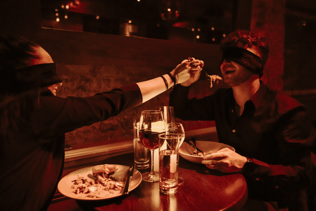 A woman feeding a blindfolded man at the Dining in the Dark experience.
