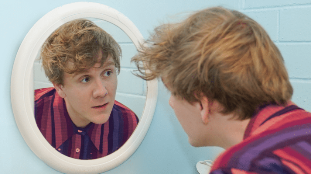a photo of comedian josh thomas standing in front of a mirror