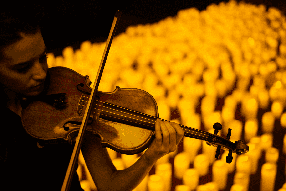 A woman playing the violin with a sea of candles behind her.