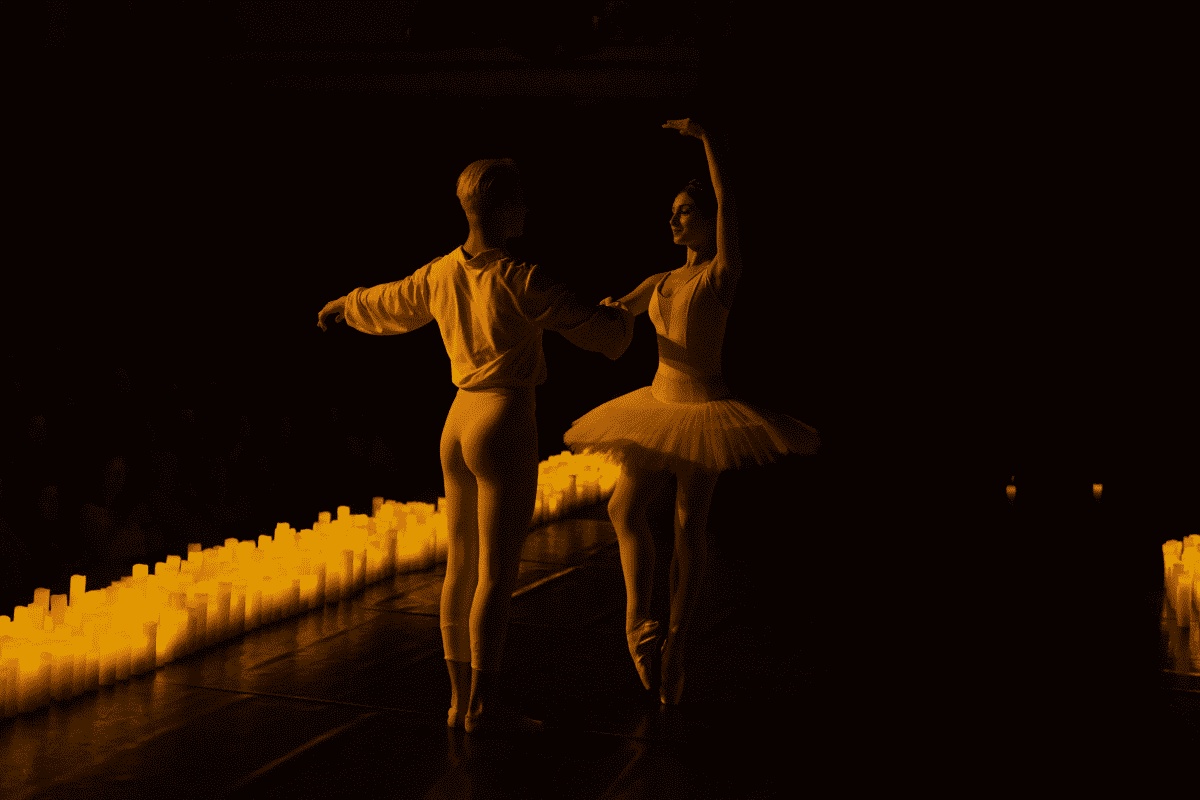 Ballerinas dancing together on a stage lined by candles.