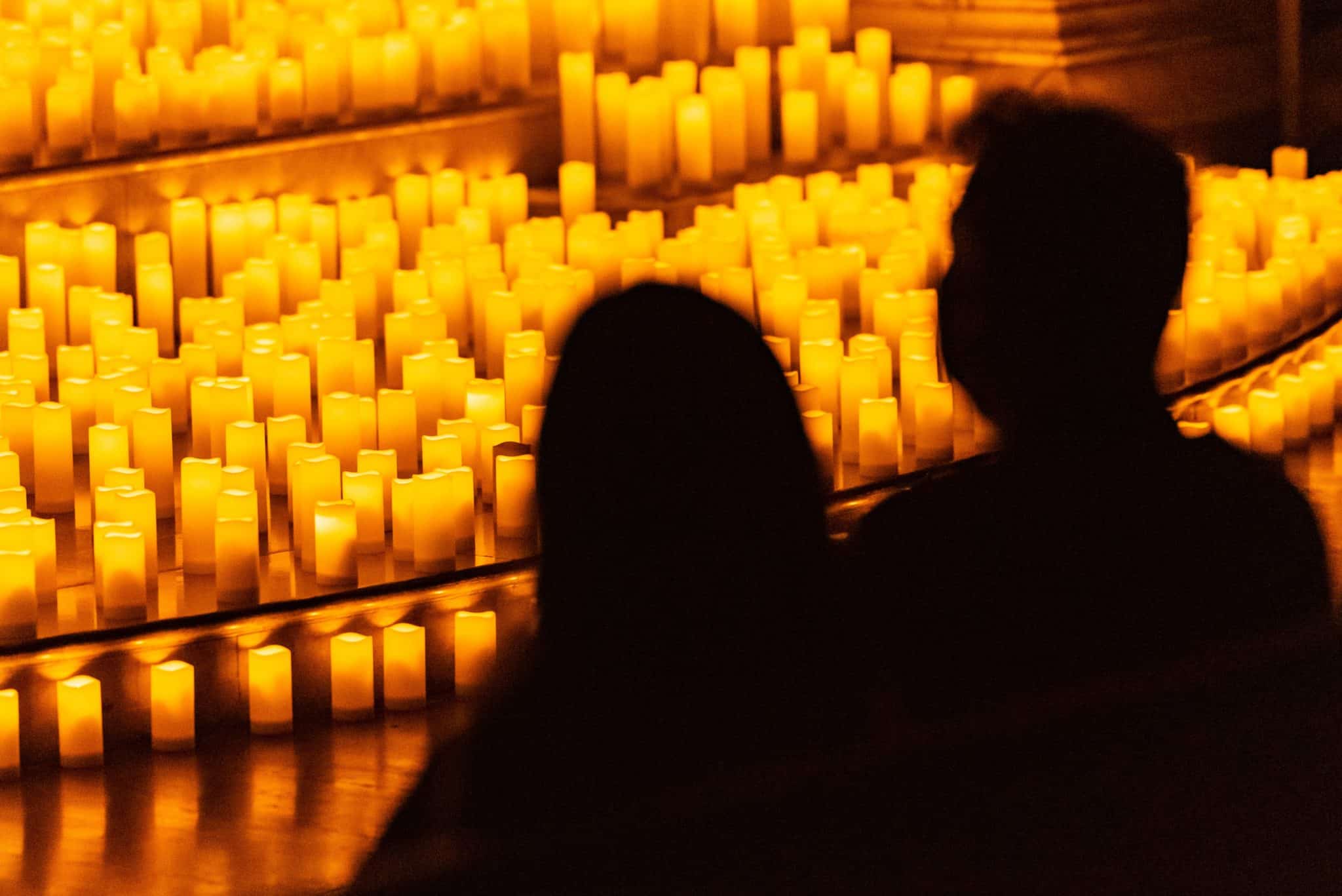 silhouette of a couple in the audience at a Candlelight concert with candles on stage