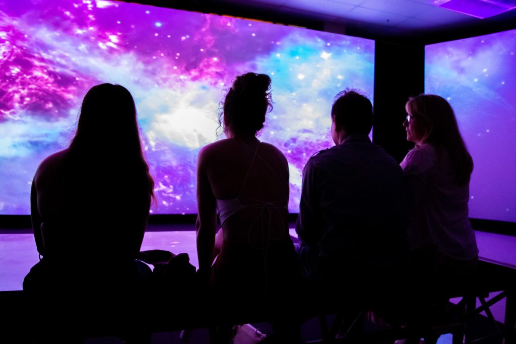 group of people sillhouette in front of projector screen image showing space and the cosmos
