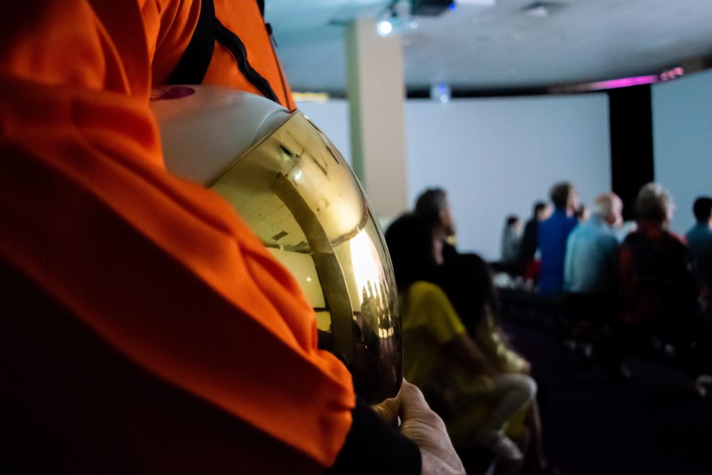 actor in astronaut suit close up on helmet in hands showing reflection of the sun at neighbourhood earth projection