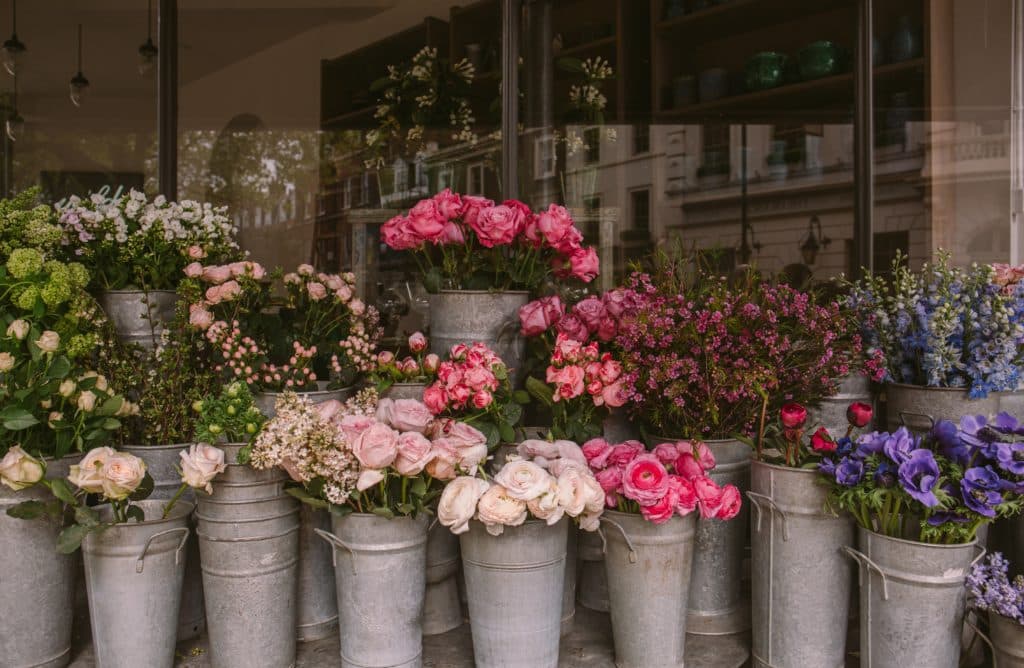 Flower stand outside a shopfront with an array of flowers (mostly roses) displayed in metal flower buckets.