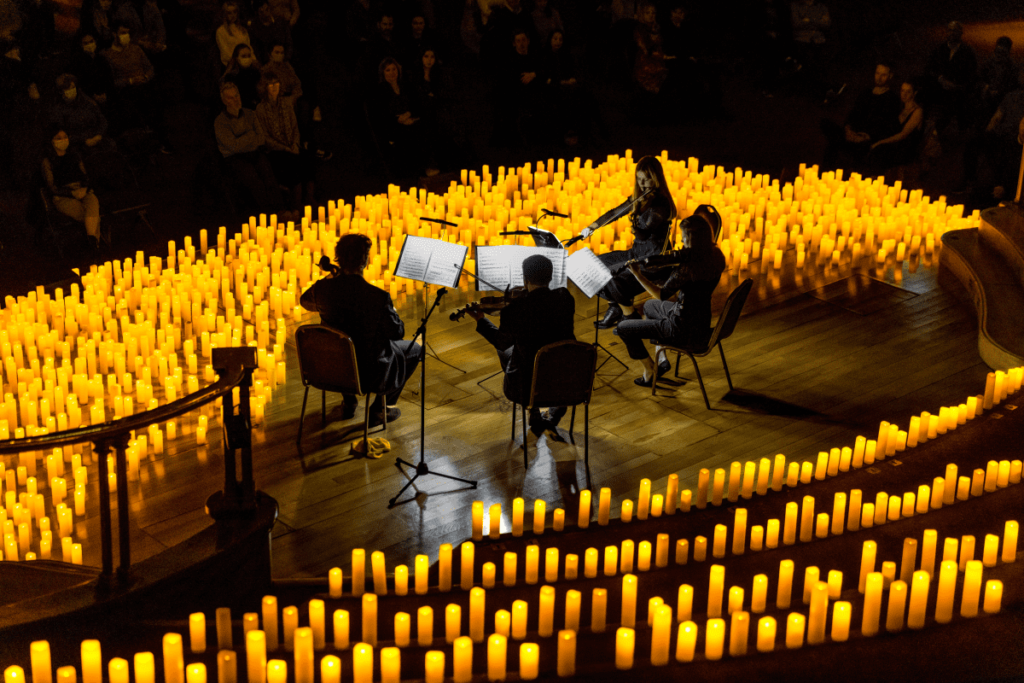 The backs of a string quartet performing on a stage surrounded by hundreds of candles.