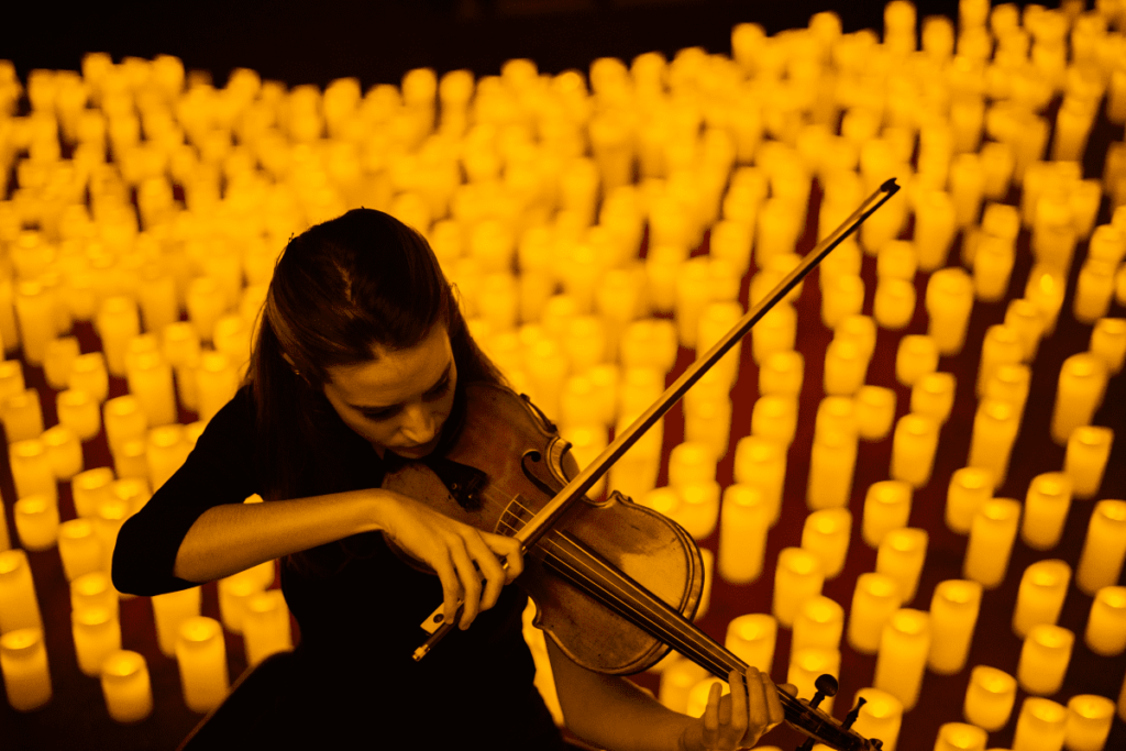 Downward shot of a violinist performing on stage surrounded by hundreds of candles