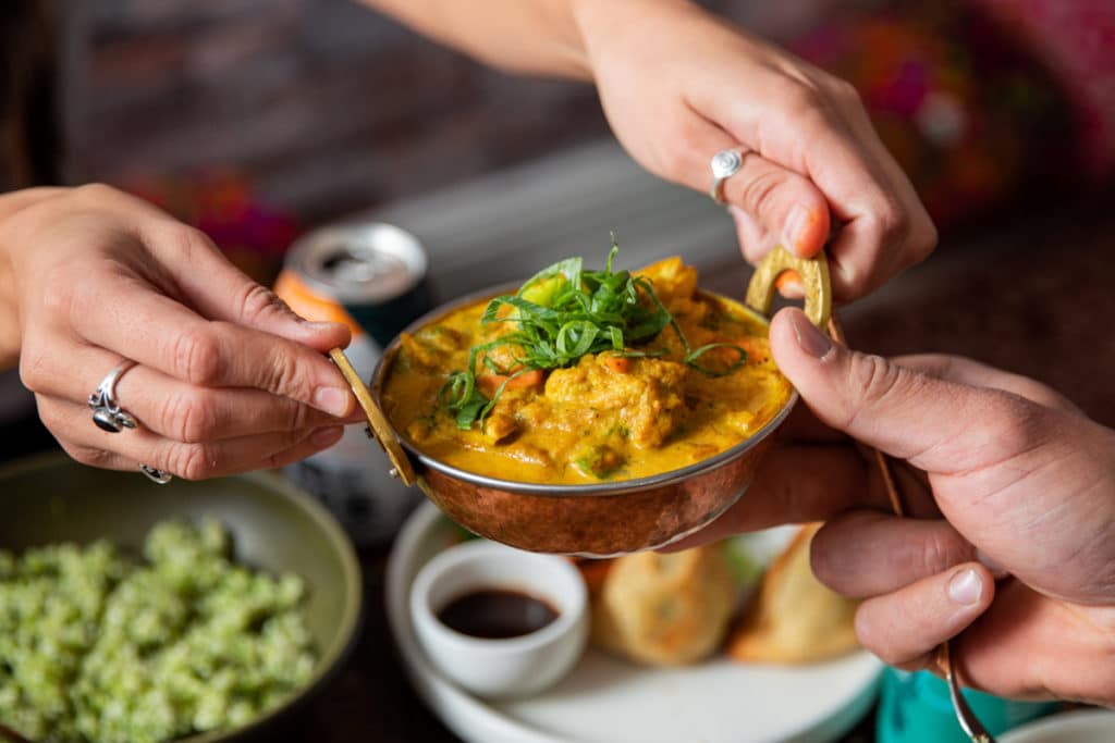 a photo of someone passing a bowl of curry to another person