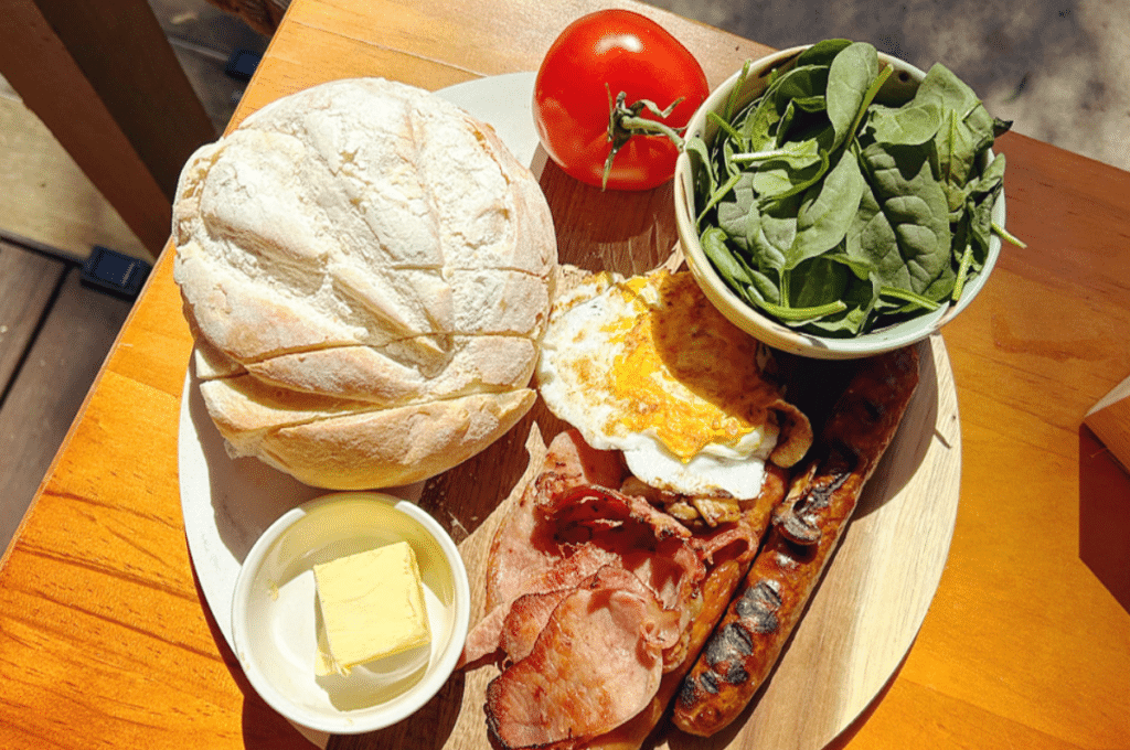 a photo of a breakfast board of bread, spinach, tomatoes, butter, eggs and bacon