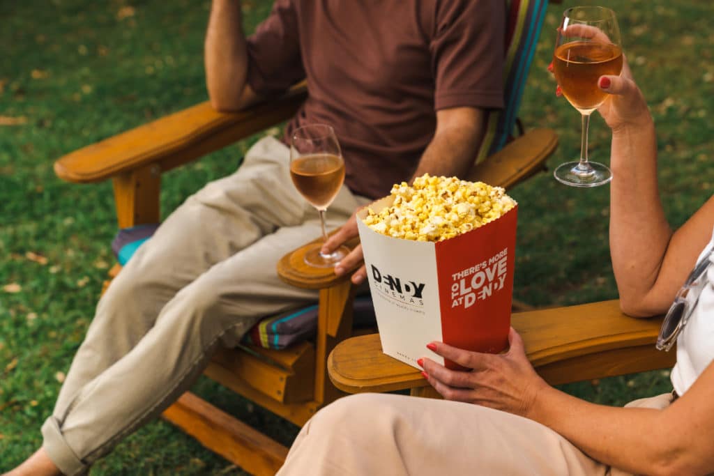 a photo of two people eating popcorn and drinking wine in outdoor arm chairs